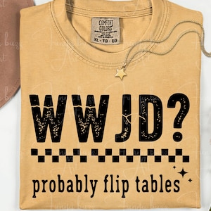 May include: Mustard-colored t-shirt with the text "WWJD? probably flip tables" in black. The shirt has a crew neck and short sleeves. A gold necklace with a star pendant is draped on the shirt.