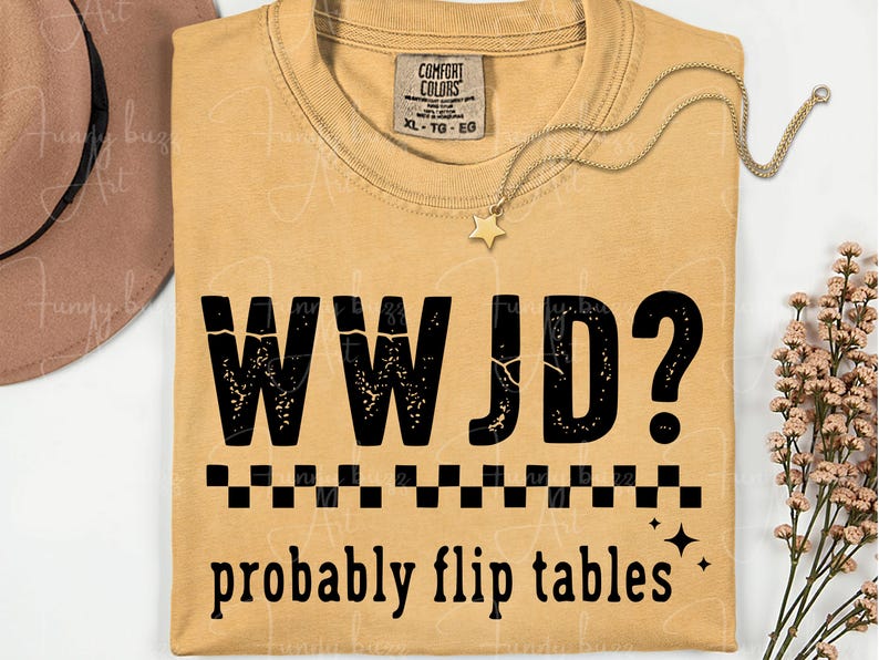 May include: Mustard-colored t-shirt with the text "WWJD? probably flip tables" in black. The shirt has a crew neck and short sleeves. A gold necklace with a star pendant is draped on the shirt.
