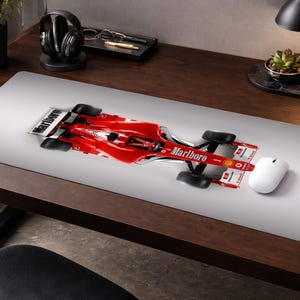 Puede incluir: Alfombrilla de ratón con un coche de carreras de Fórmula 1 rojo y blanco con el logotipo "Marlboro". La alfombrilla está sobre un escritorio de madera con un ratón blanco, auriculares y una planta.