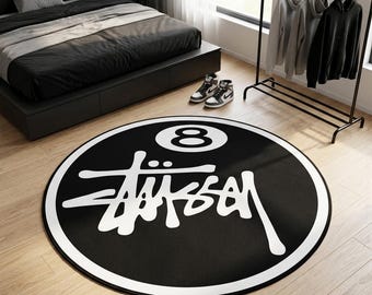 May include: A circular black rug featuring a large white graphic of the number eight inside a circle, positioned above the white stylised text "Stussy". The rug has a thick white border around the entire circumference, creating a high-contrast design.