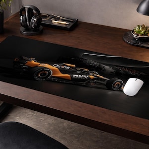 May include: Black rectangular desk mat featuring a Formula 1 race car in orange and black. The car has the word "Chrome" on the side. A white computer mouse is next to the car.