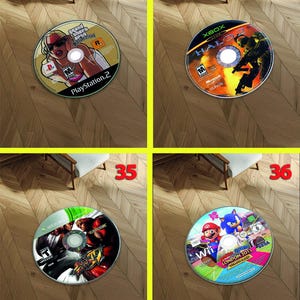 May include: Four video game discs are displayed on a wooden floor. The discs include titles like "Grand Theft Auto: San Andreas" for PlayStation 2, "Halo 2" for Xbox, "Street Fighter X Tekken" for Xbox, and "Mario & Sonic at the London 2012 Olympic Games" for Wii.