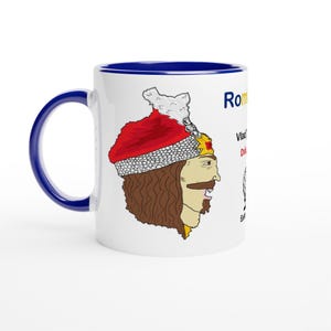 May include: White ceramic mug with a blue interior and handle. The mug features a cartoon illustration of a historical figure wearing a red hat and a gold-colored collar. Text on the mug includes the word "Romania" and other text.