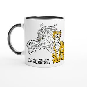 Peut inclure: Mug en céramique blanche avec une anse et un bord noirs. La tasse présente une illustration détaillée d'un tigre et d'un dragon, avec du texte japonais en dessous. Le tigre est jaune et noir, et le dragon est blanc.