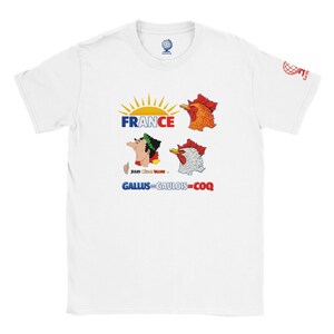 Peut inclure: Un t-shirt blanc à manches courtes avec un imprimé graphique comprenant le texte FRANCE, une icône de soleil, deux têtes de coq et un profil de Jules César. En dessous, le texte indique GALLUS=GAULOIS=COQ. Un petit logo globe est sur la manche.