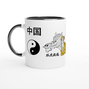 Peut inclure: Mug en céramique blanche avec une anse et un bord noirs. Le mug présente un symbole yin-yang noir et blanc, des caractères chinois et un dessin d'un tigre et d'un dragon. Le design du mug est un mélange d'éléments culturels orientaux.
