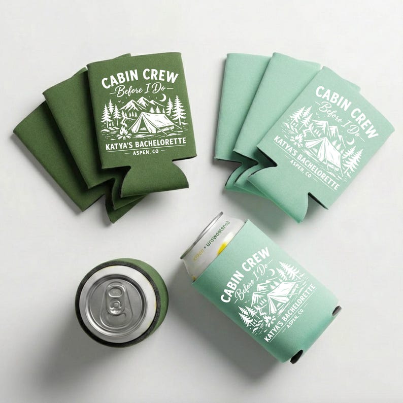 May include: Green and mint-colored can coolers with the text "CABIN CREW - Before I Do" and "KATYA'S BACHELORETTE - ASPEN, CO" printed in white. One cooler holds a can. The design features a tent, trees, and mountains.