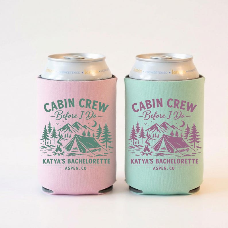 May include: Two can coolers, one pink and one teal, each featuring a camping-themed design. The text reads "CABIN CREW - Before I Do - KATYA'S BACHELORETTE - ASPEN, CO" in a forest green and purple color scheme. The design includes a tent, mountains, trees, and a campfire.