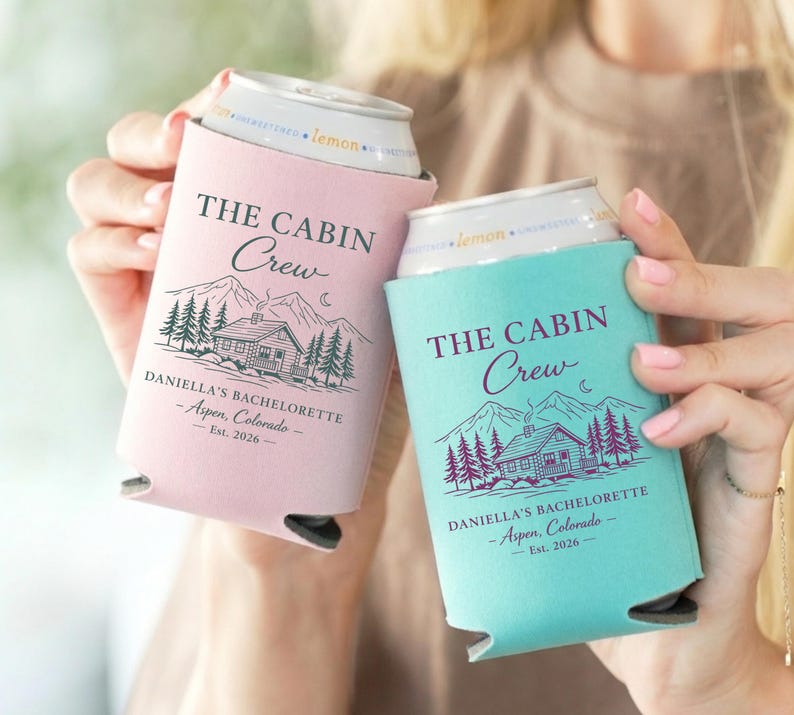 May include: Two can coolers, one pink and one teal, each with the text "THE CABIN Crew" and a cabin graphic. The text "DANIELLA'S BACHELORETTE - Aspen, Colorado - Est. 2026" is also printed on the coolers.