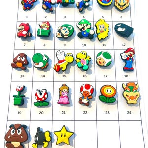 May include: A collection of thirty colourful rubber shoe charms featuring various Super Mario characters and icons, including Mario, Luigi, Princess Peach, Bowser, Goombas, and power-ups, arranged in a numbered grid on a white background.