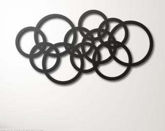 Pode incluir: Arte de parede em metal preto com um design de círculos sobrepostos. A escultura abstrata é montada numa parede branca, criando uma estética moderna e minimalista. Os círculos variam em tamanho e sobrepõem-se para um efeito visual dinâmico.