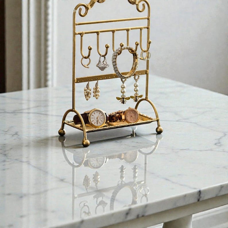 May include: A gold-colored metal jewelry organizer with a decorative top and curved base. The organizer holds various earrings, rings, bracelets, and watches. The watches are displayed on a small tray at the base of the organizer.