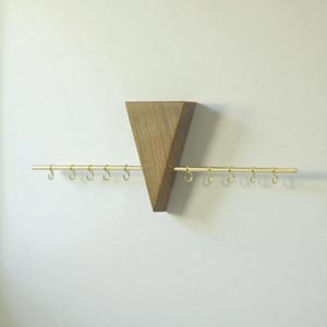 May include: A wooden wall-mounted jewellery organiser with a triangular design. The organiser features a natural wood finish and a horizontal brass bar with small hooks for hanging necklaces or bracelets. The design is minimalist and modern.