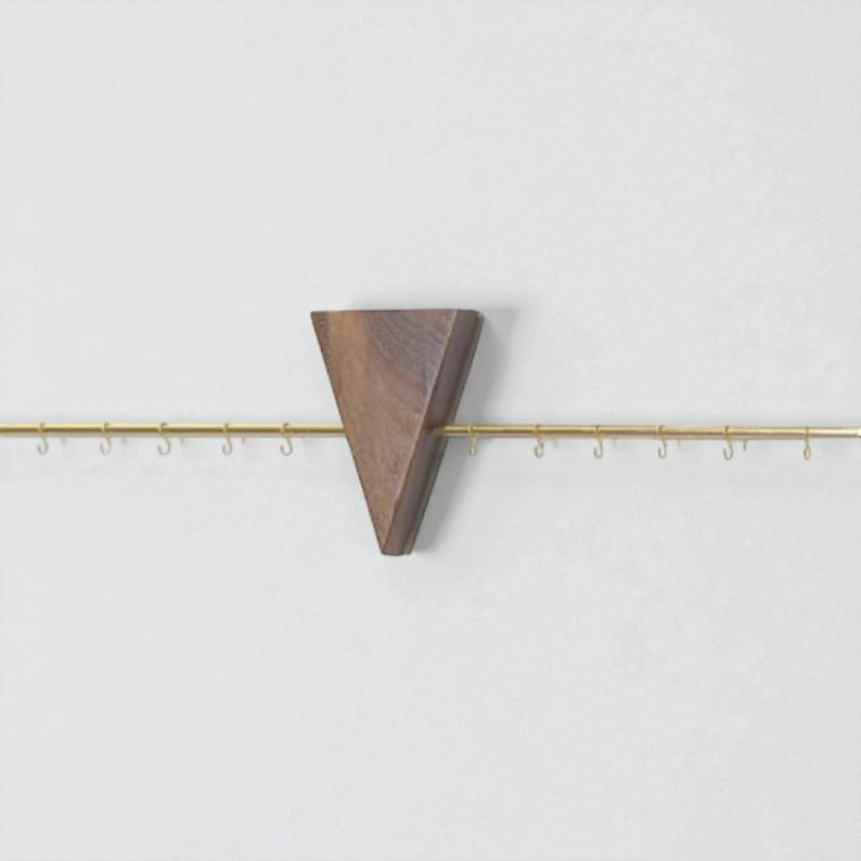 May include: A wall-mounted jewellery organiser featuring a triangular wooden accent piece and a brass rod with small hooks. The wooden piece is a dark brown colour, and the hooks are evenly spaced along the rod.