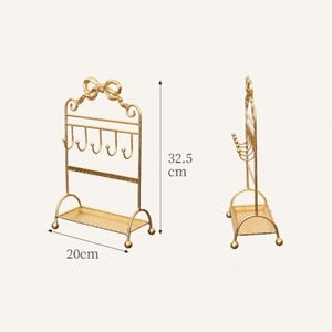 May include: A gold-colored jewelry display stand with a bow-shaped top and multiple hooks for hanging necklaces and bracelets. The stand is 12.8 inches tall and 7.9 inches wide, with a small shelf at the base for additional storage.
