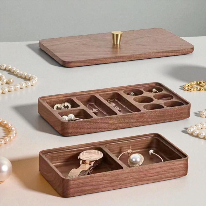 K&ouml;nnte beinhalten: Ein h&ouml;lzerner Schmuckorganizer mit rechteckiger Form und mehreren F&auml;chern. Der Organizer ist aus dunkelbraunem Holz gefertigt und hat einen passenden Deckel mit einem goldfarbenen Knopf. Die F&auml;cher enthalten verschiedene Schmuckst&uuml;cke, darunter Halsketten, Ohrringe und eine Uhr.
