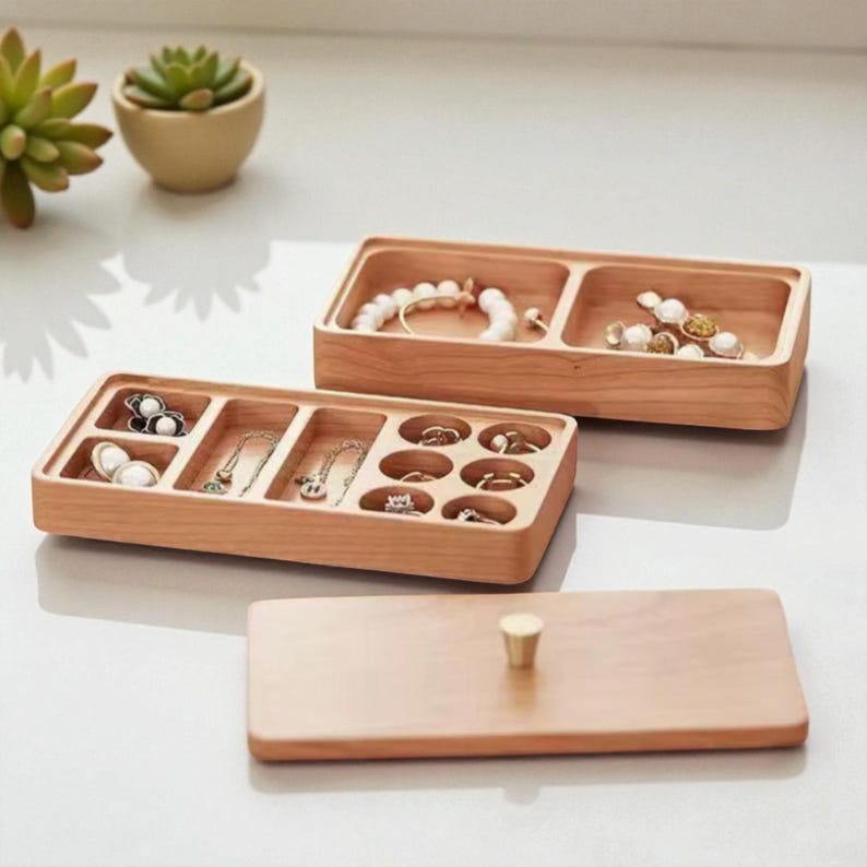 K&ouml;nnte beinhalten: Hellbrauner Schmuck-Organizer aus Holz mit mehreren F&auml;chern. Der Organizer enth&auml;lt Armb&auml;nder, Halsketten und Ringe. Ein passender Deckel mit goldenem Knopf ist ebenfalls vorhanden.