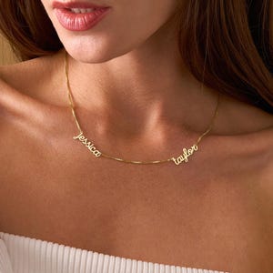 May include: A delicate gold necklace featuring the names "Jessica" and "Taylor" in a cursive font. The necklace is worn around the neck, showcasing the personalized design. The chain is a fine, subtle link.