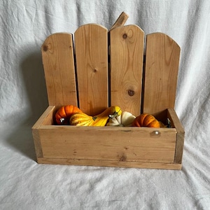 May include: A wooden pumpkin-shaped planter with a box base and a slatted back. The planter is filled with small gourds in shades of orange, yellow, and white. The wood has a natural finish, and the planter sits on a white surface.
