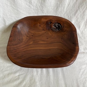 May include: A dark brown wooden serving tray with a natural finish. The tray has an irregular, organic shape with rounded edges and a knot feature. The wood grain is visible, enhancing its rustic appeal. Ideal for serving food or displaying decorative objects.