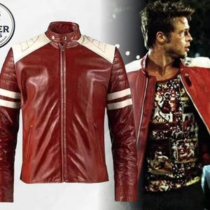 May include: A red leather jacket featuring a stand-up collar with a snap button, white shoulder panels, and two horizontal white stripes on each sleeve. The jacket includes a central zipper closure and two side pockets. A logo reads JACKER CRAFTS.