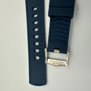 Puede incluir: Dos piezas de una correa de reloj azul oscuro con un patr&oacute;n de ondas texturizadas. Una pieza tiene una serie de agujeros ovalados. La otra pieza tiene una hebilla de acero inoxidable con el texto "STAINLESS STEEL ST2010129 11 HIC".