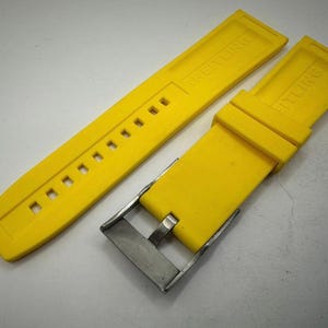 Puede incluir: Correa de reloj de color amarillo brillante con el nombre de la marca impreso en la correa. La correa tiene una serie de agujeros para ajustar y una hebilla de acero inoxidable. La correa est&aacute; hecha de un material flexible.