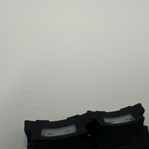 May include: Close-up of two black plastic components with a curved design and a rectangular opening. The components are set against a plain, light gray background. The image is well-lit, highlighting the details of the plastic.