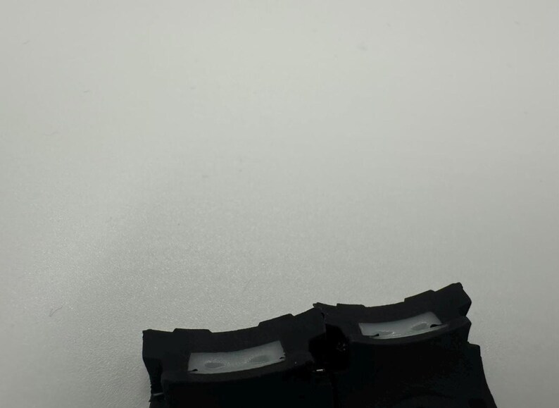 May include: Close-up of two black plastic components with a curved design and a rectangular opening. The components are set against a plain, light gray background. The image is well-lit, highlighting the details of the plastic.