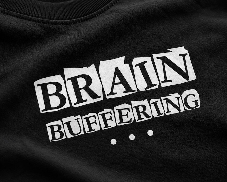 May include: A black t-shirt featuring the white text BRAIN BUFFERING with three dots below it. The letters are presented in a ransom note style with individual white rectangular backgrounds for each letter, creating a high-contrast graphic design.