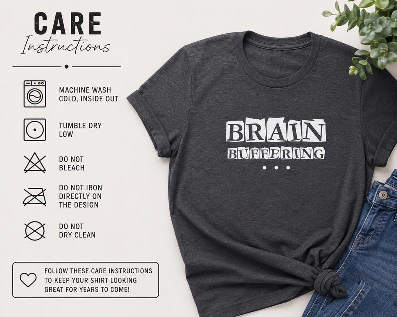 May include: A dark charcoal gray t-shirt featuring the white text BRAIN BUFFERING with three dots below. To the left, a care instruction chart lists machine wash cold, tumble dry low, do not bleach, do not iron on design, and do not dry clean.