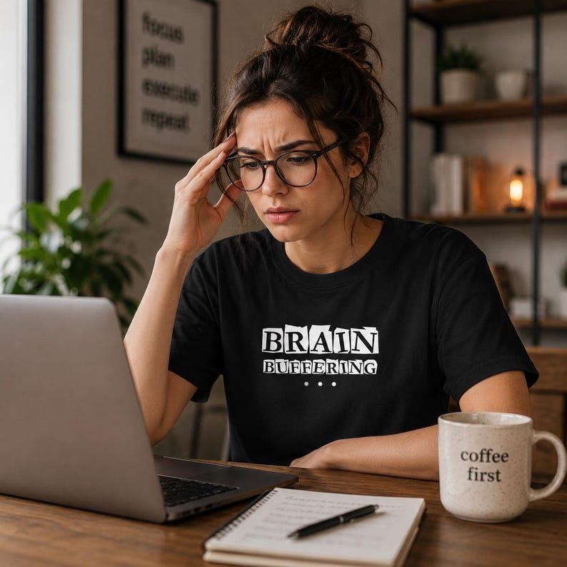 May include: A black short-sleeved t-shirt featuring the white text "BRAIN BUFFERING" with three dots underneath. The graphic is centered on the chest of the garment, which is made of a solid black fabric with a standard crew neckline and short sleeves.