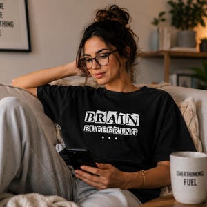 May include: A black short-sleeved t-shirt featuring the white text "BRAIN BUFFERING" with three dots underneath. The shirt has a crew neckline and a relaxed fit. The design is printed in a bold, blocky font style across the center of the chest.