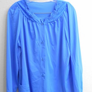 May include: A light blue pajama set with a button-up top and long pants. The top has a decorative floral trim around the neckline.