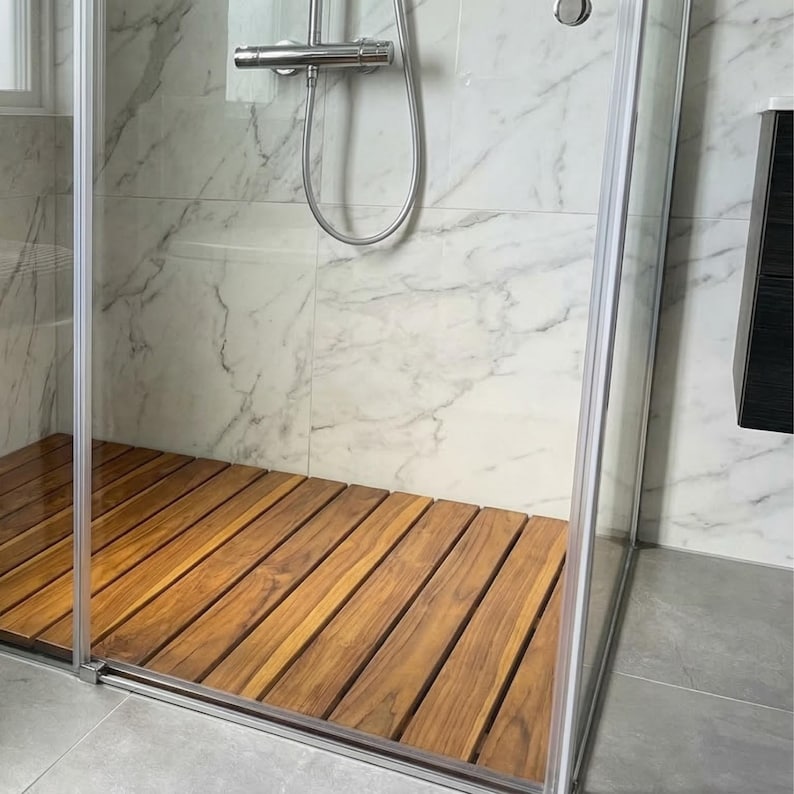 May include: A modern shower enclosure with a wooden floor. The shower features a clear glass door and a stainless steel shower head. The floor is made of wooden planks, adding a natural element to the bathroom.