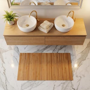 K&ouml;nnte beinhalten: Ein moderner Badezimmerwaschtisch mit zwei wei&szlig;en, runden Waschbecken und goldenen Wasserh&auml;hnen. Der Waschtisch ist aus hellem Holz gefertigt und hat zwei Schubladen. Eine Bambus-Badematte liegt auf dem Marmorboden. Eine kleine Pflanze und gefaltete Handt&uuml;cher sind ebenfalls zu sehen.