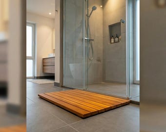 Könnte beinhalten: Eine rechteckige Badezimmermatte aus Holz, bestehend aus parallelen Lamellen in natürlichem Braun, die auf einem grauen Fliesenboden direkt vor einer verglasten Duschkabine mit verchromter Duschbrause und Armaturen liegt.