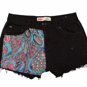 May include: Black denim shorts with a unique design. The left side features a colorful, patterned fabric with blue, pink, and purple embroidery. The shorts have a frayed hem and the Levi's logo is visible.