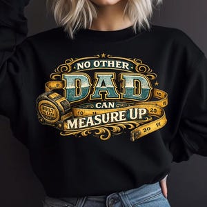 May include: A black long-sleeve sweatshirt featuring a graphic design with the text NO OTHER DAD CAN MEASURE UP. The design includes a yellow measuring tape wrapped around the text and a tape measure tool labelled BUILT TO LAST in gold.