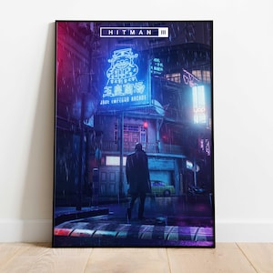 May include: A framed art print featuring a neon-lit street scene from the video game Hitman III. The artwork depicts a person walking in the rain, with vibrant neon signs in Chinese characters and a retro aesthetic.
