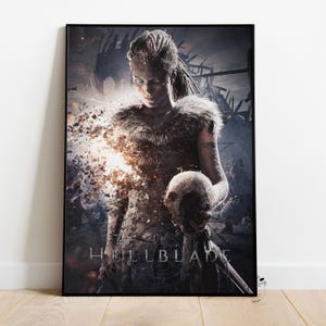 May include: A framed poster featuring a character from the video game Hellblade. The character is a woman with a determined expression, holding a skull. The poster has a dark, dramatic aesthetic with a focus on the character and the game's title.
