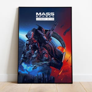 Puede incluir: Un póster enmarcado del videojuego "Mass Effect: Legendary Edition". La obra de arte muestra varios personajes con atuendos futuristas, ambientados en un fondo espacial con tonos rojos y azules. El título del juego se muestra en la parte superior.
