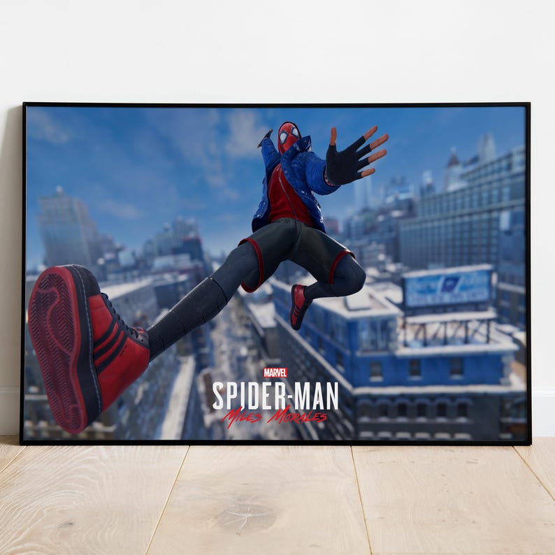 May include: A framed poster featuring the Marvel character Spider-Man in a dynamic pose. The character is wearing a red and black suit with a blue jacket, mid-air against a cityscape backdrop. The Marvel Spider-Man Miles Morales logo is visible.