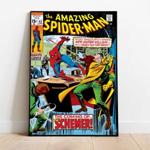 May include: A framed comic book cover of The Amazing Spider-Man. The cover features Spider-Man in a red and blue suit, battling a villain in a yellow cape and green suit. Text includes "The Coming of... The Schemer!"