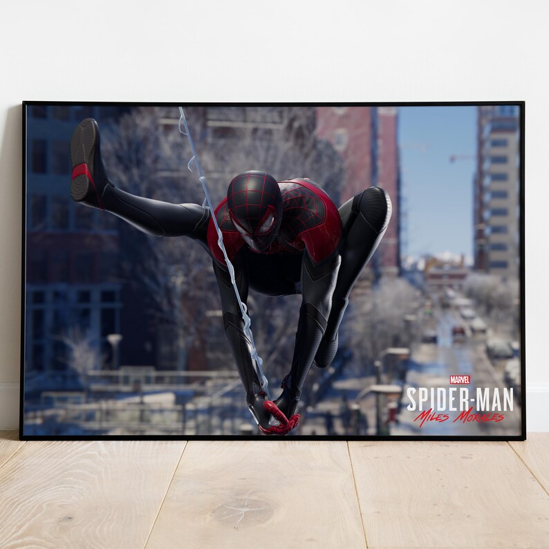 May include: A framed poster featuring the character Spider-Man in a dynamic pose. The superhero is clad in a black and red suit, with a web extending from his hand. The background shows a city street, and the Marvel logo is visible.