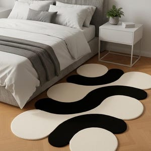 May include: A modern bedroom scene featuring a black and white abstract rug. The rug has a unique, flowing design with circular and wave-like shapes. The room includes a bed with white bedding and a gray headboard, and a white nightstand.
