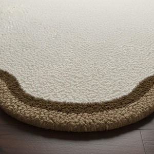 May include: Close-up of a cream-colored, textured rug with a wavy border. The border features two bands of brown and tan colors. The rug is placed on a dark brown wooden floor.