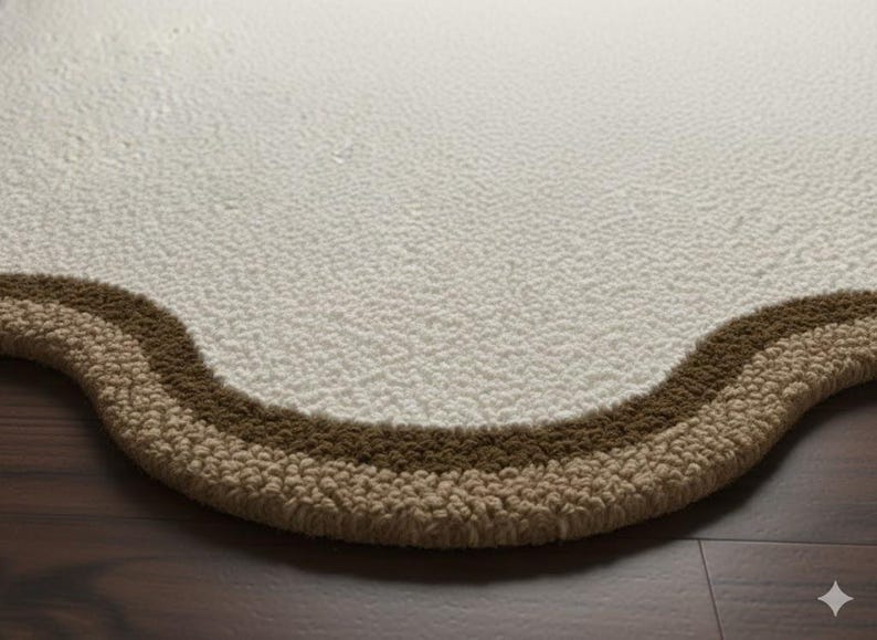 May include: Close-up of a cream-colored, textured rug with a wavy border. The border features two bands of brown and tan colors. The rug is placed on a dark brown wooden floor.
