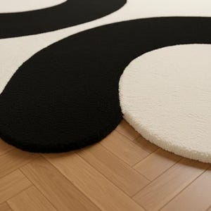 May include: A modern, abstract rug featuring a bold black and off-white design. The rug has a soft, textured surface and a unique, flowing pattern. The contrasting colors and organic shapes create a stylish accent for any room.