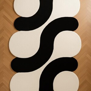 May include: A modern area rug with a bold, abstract design. The rug features a pattern of interconnected shapes in black and off-white. The design includes large, rounded forms that create a striking visual contrast, suitable for contemporary interiors.